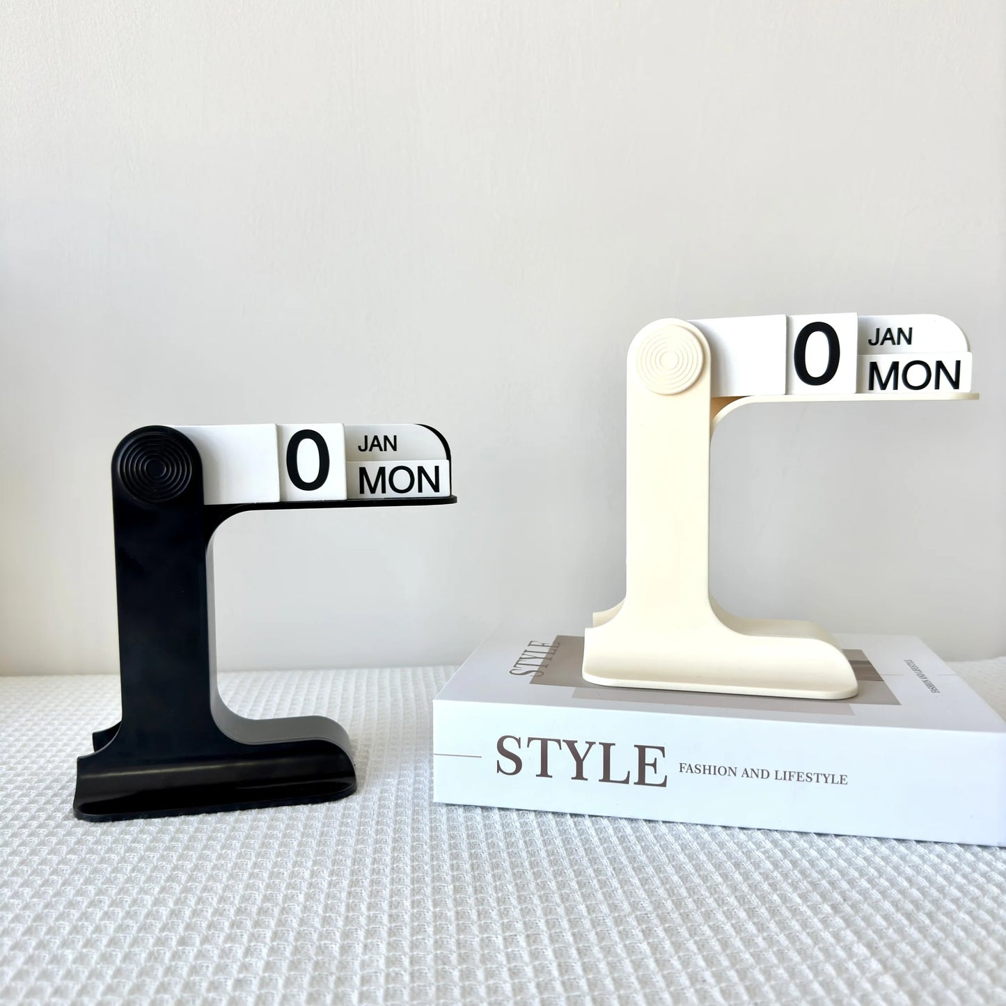 Two black and white calendar stands on a textured surface with a 'STYLE' book in the background.