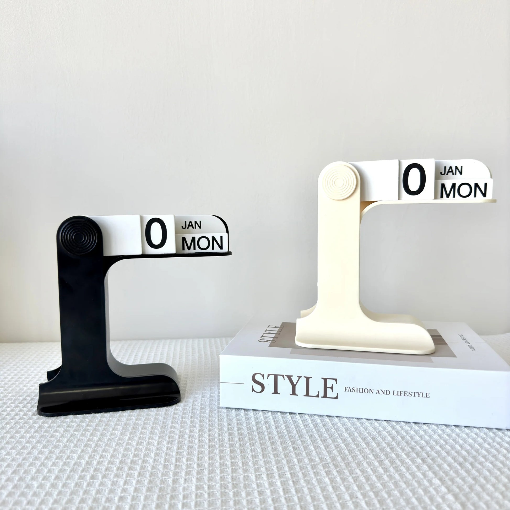 Two black and white calendar stands on a textured surface with a 'STYLE' book in the background.