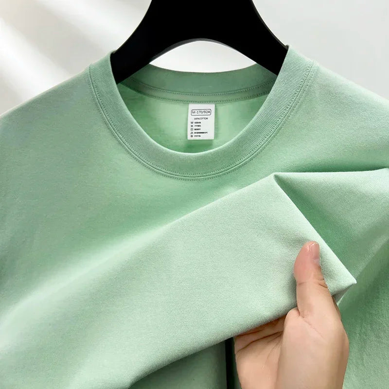 Light green t-shirt held by a hand with a hanger on a white background