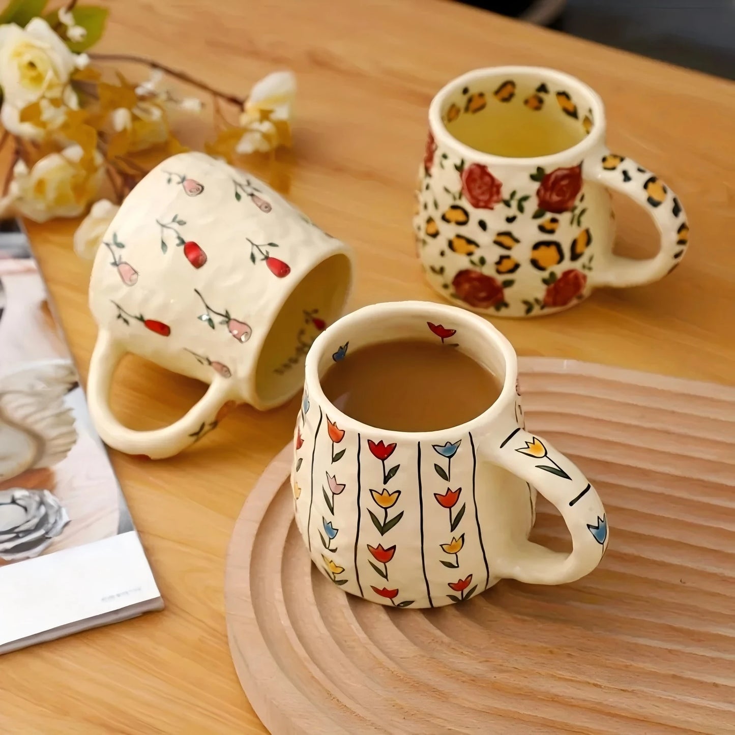 Three ceramic mugs with floral and leopard print designs on a wooden table.