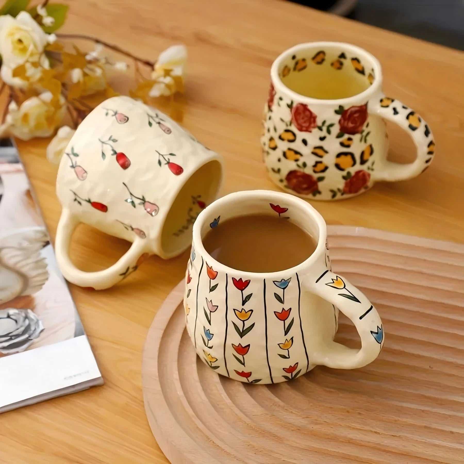 Three ceramic mugs with floral and leopard print designs on a wooden table.