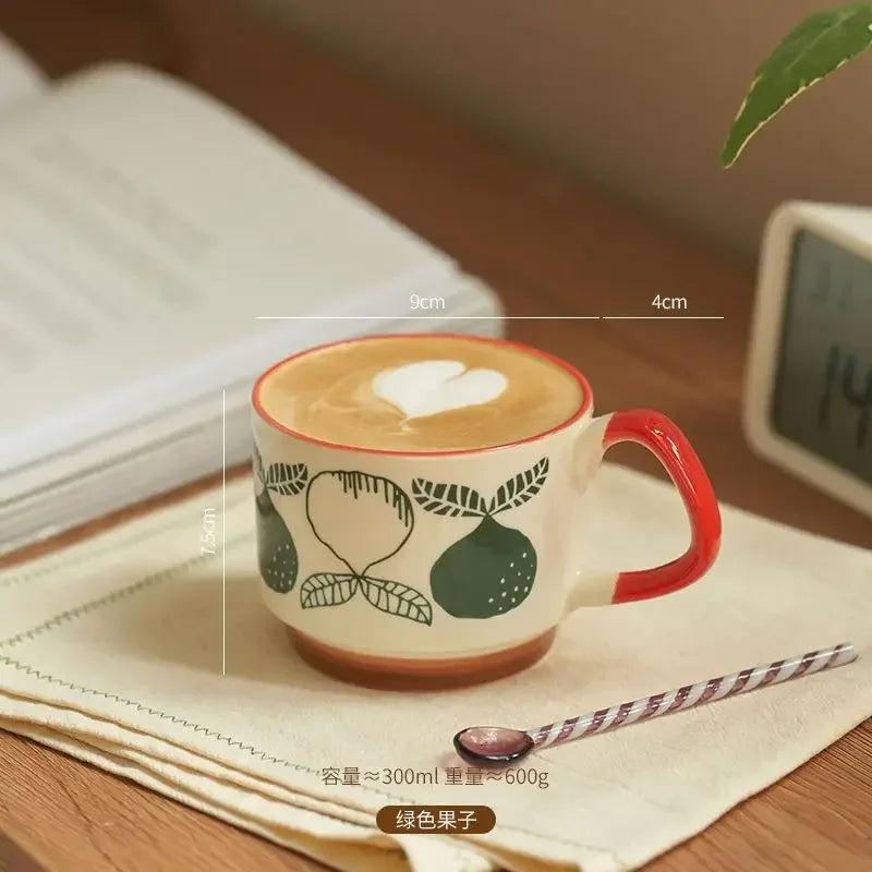Ceramic mug with green fruit design on a wooden table with a book and digital clock in the background.