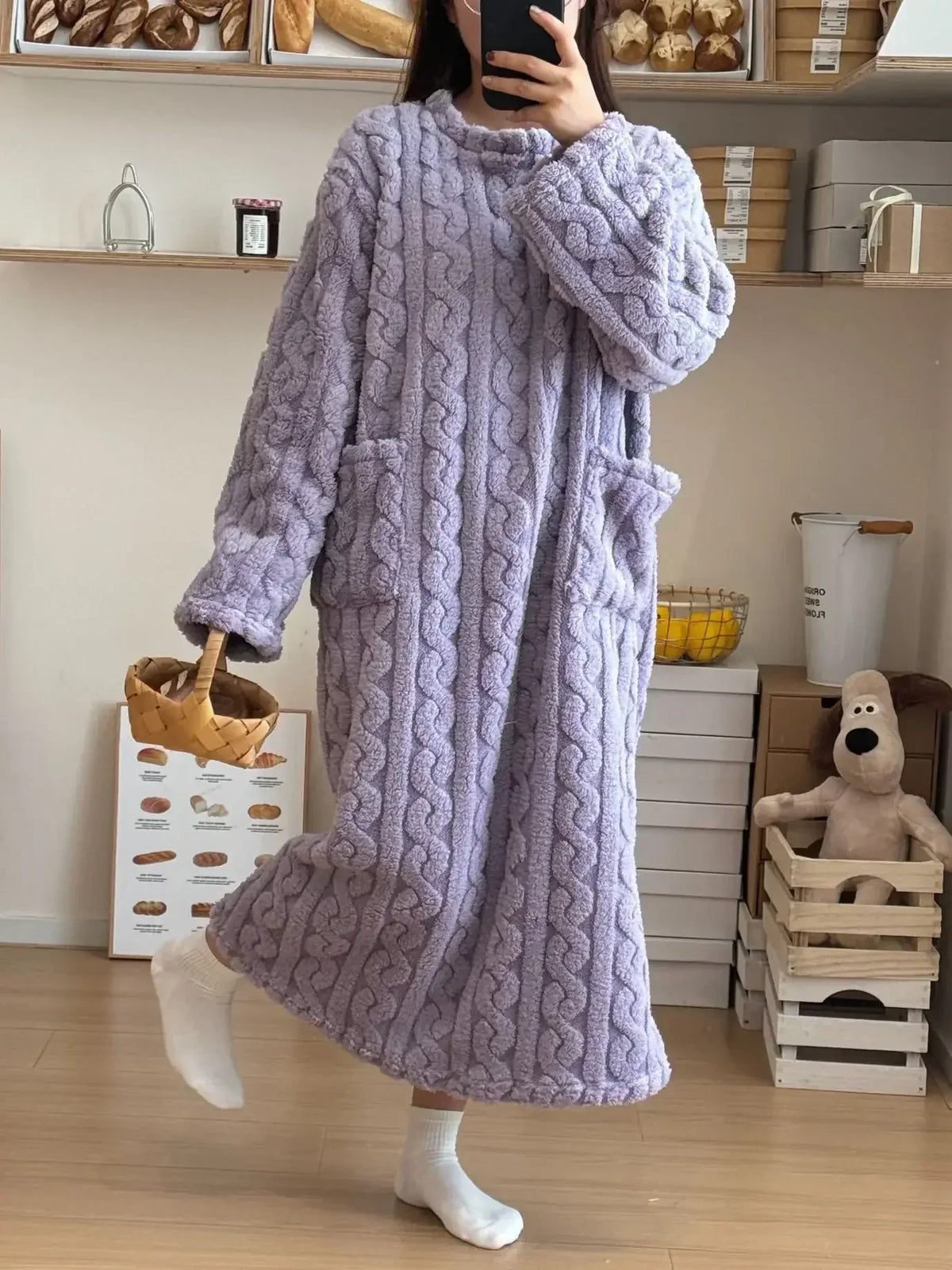 Person wearing a textured purple robe in a room with shelves and a plush toy.