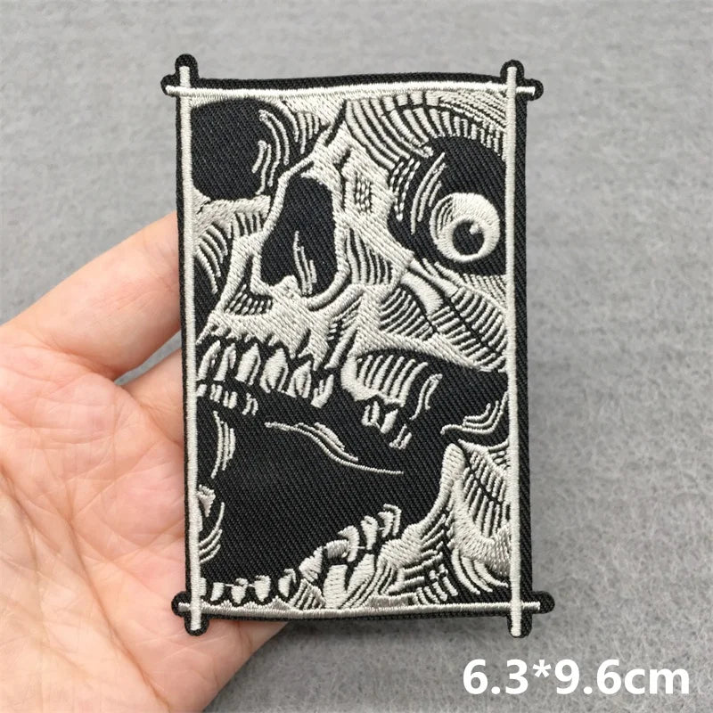 Black and white embroidered patch of a skull held by a hand on a gray background