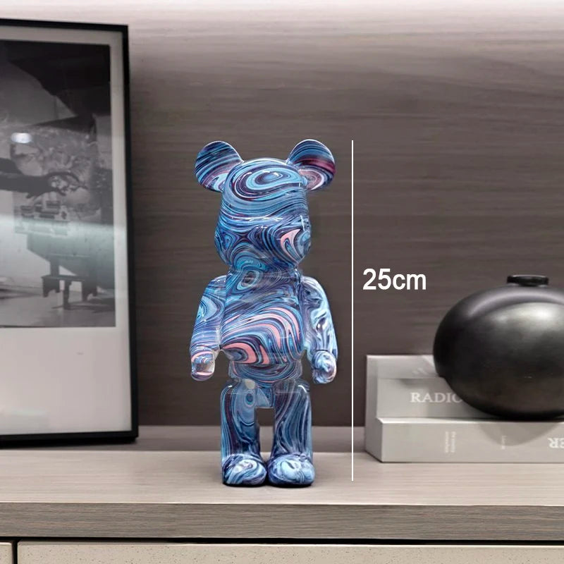 A translucent bear-shaped collectible figure with a blue, purple, and pink marbled swirl pattern, standing on a shelf with a 25cm height marker overlay. The background shows a framed black-and-white print, a black decorative vase on books, and a gray wood-grain wall.
