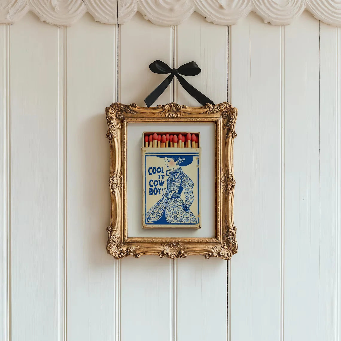 Decorative framed artwork with a vintage matchbox design on a paneled wall.