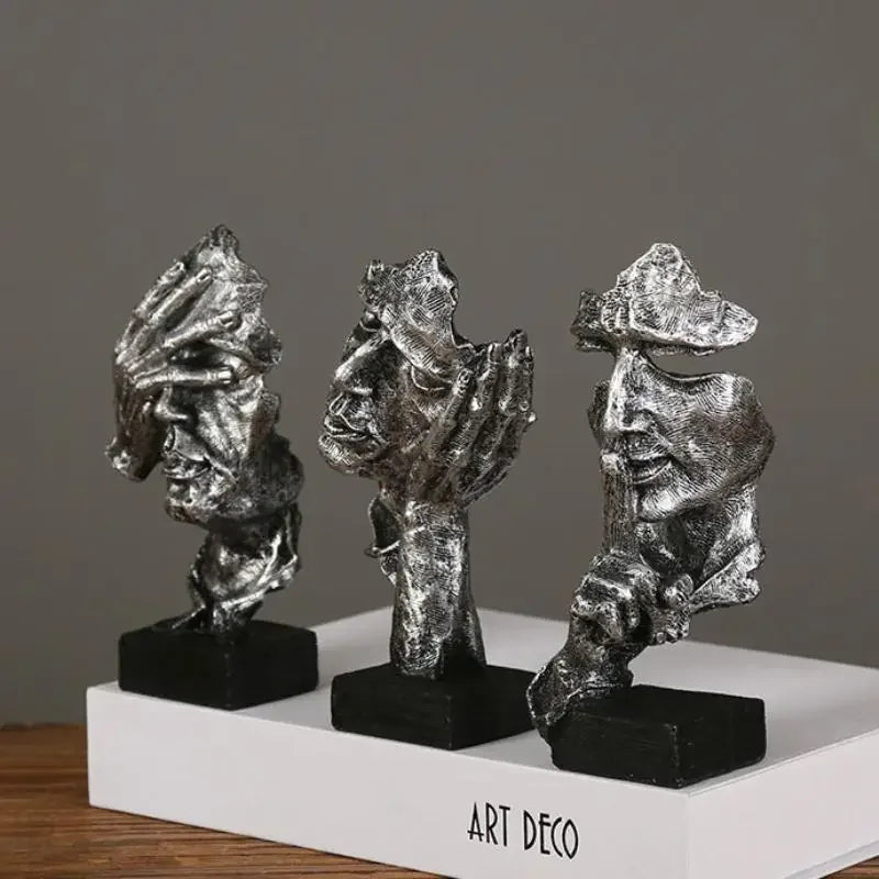 Three artistic sculptures on a wooden surface in silver on a white surface and grey background