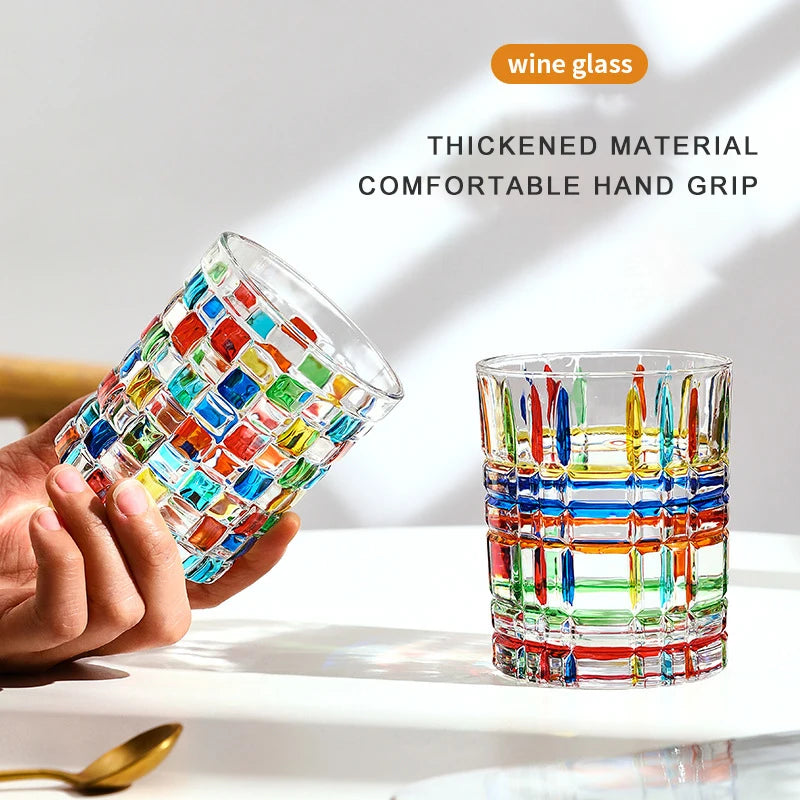 Colorful glass wine glasses with a hand holding one, on a light background.