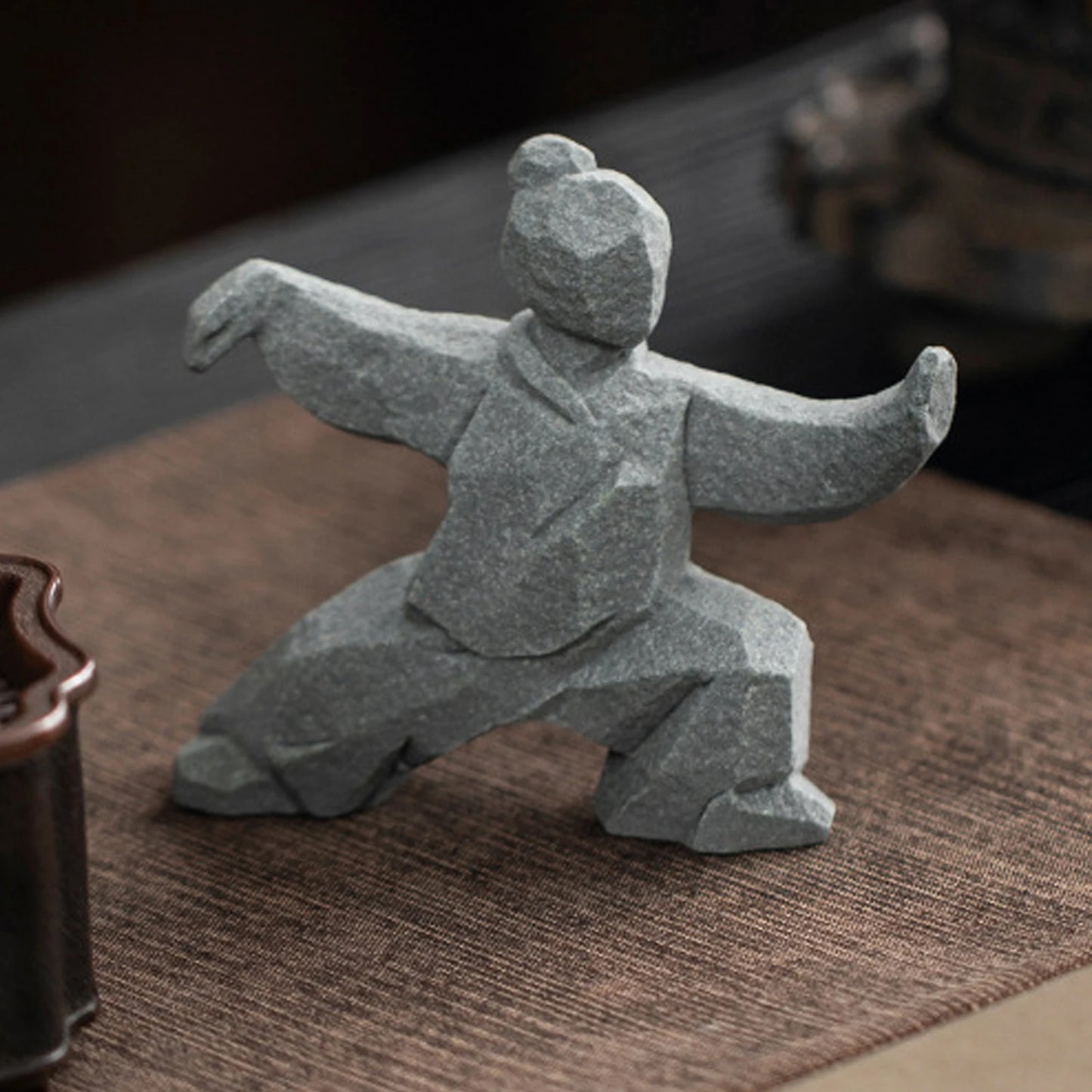 Stone sculpture of a martial artist in a dynamic pose on a textured surface.