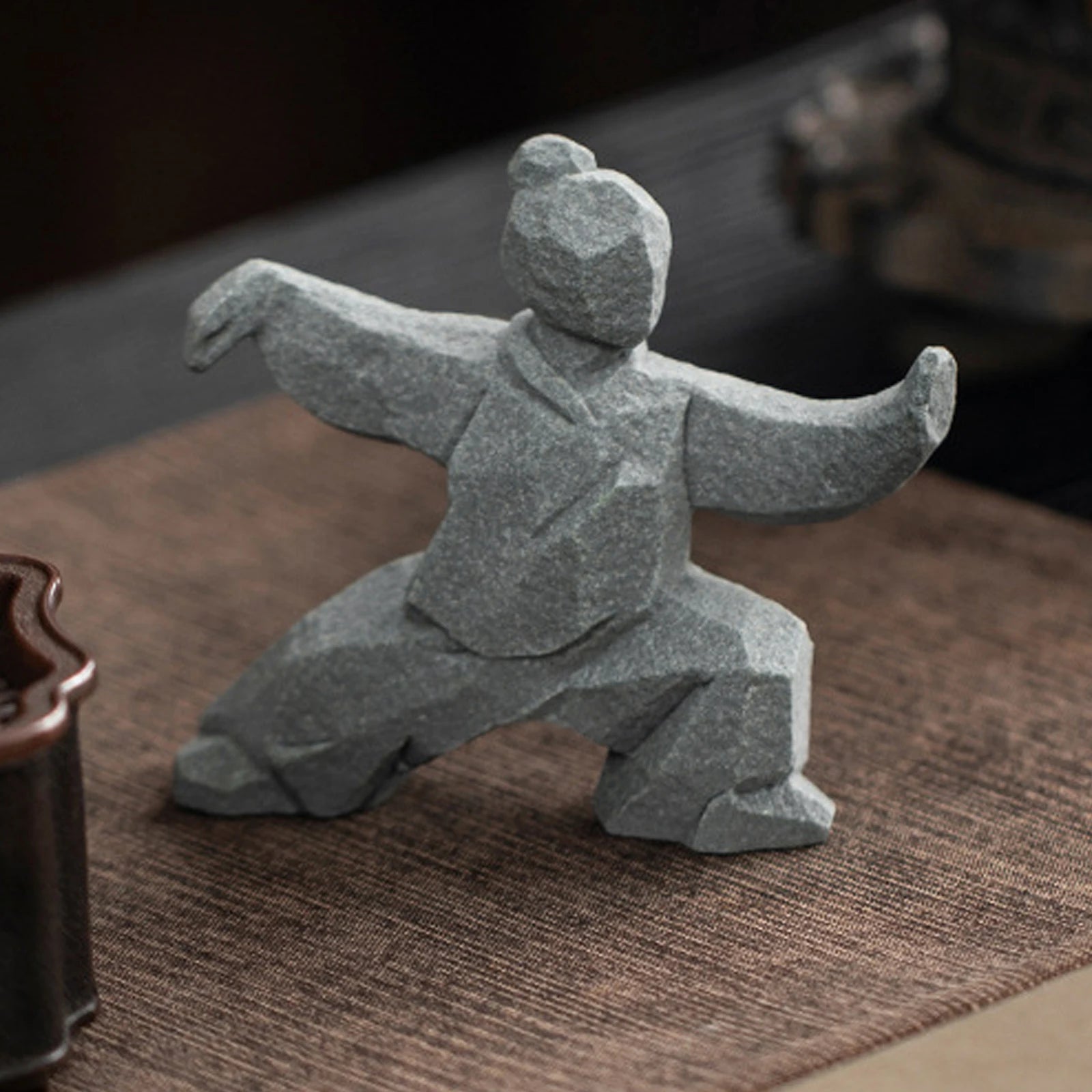 Stone sculpture of a martial artist in a dynamic pose on a textured surface.