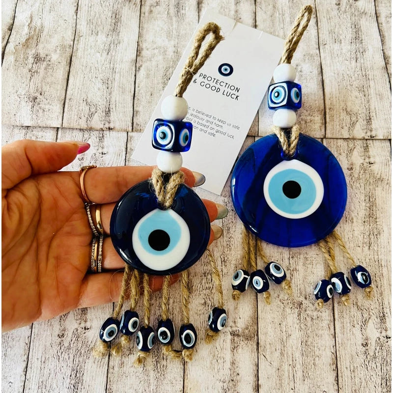 Evil eye ornaments with a hand holding one, on a wooden surface.