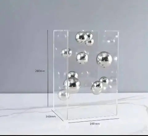 Clear acrylic box with silver spherical objects on a gray background