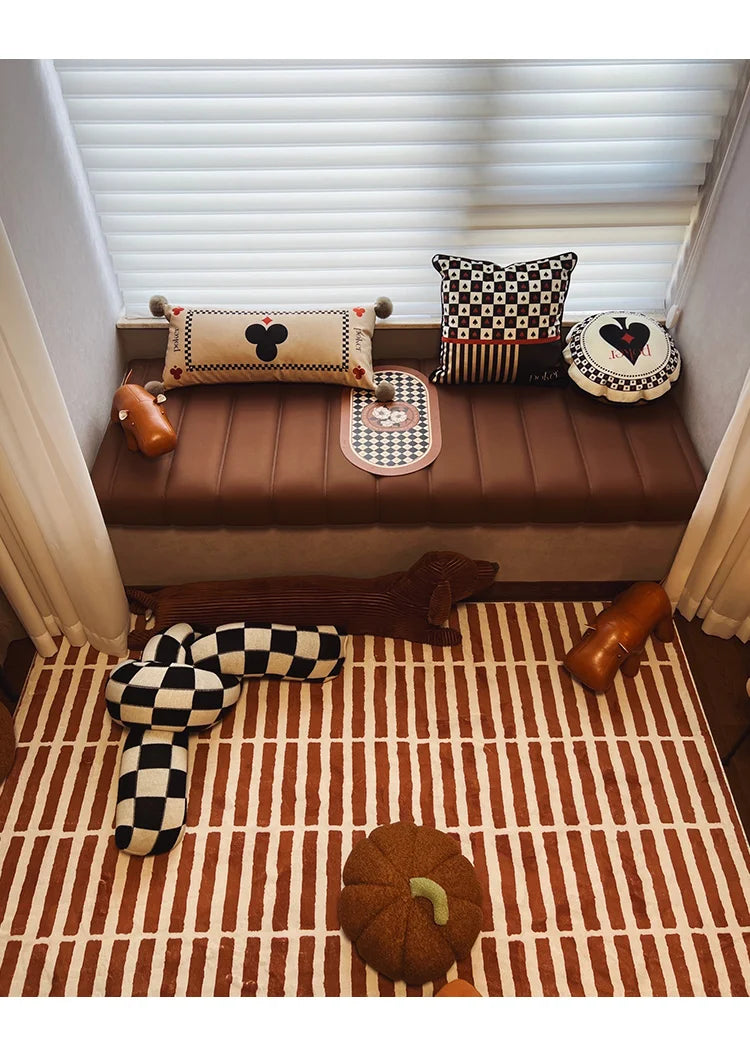 Decorative nook with cushions and a checkered pillow on a striped rug.