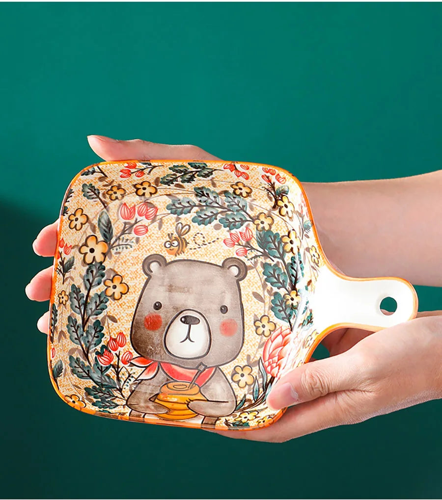 Ceramic tray with bear design held by a hand against a green background