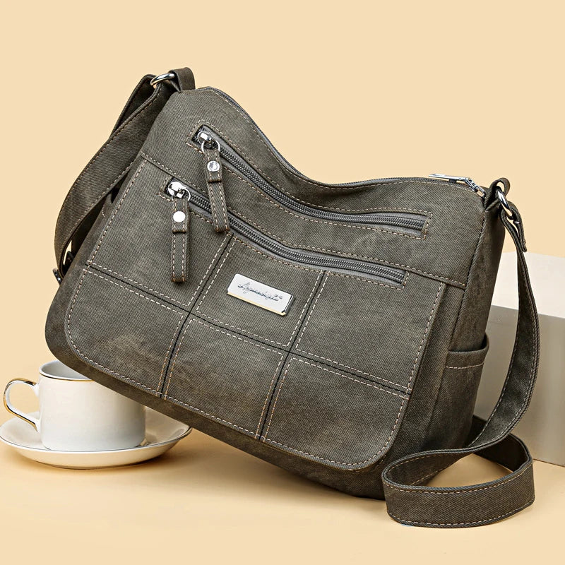 Gray shoulder bag with multiple zippers on a beige background