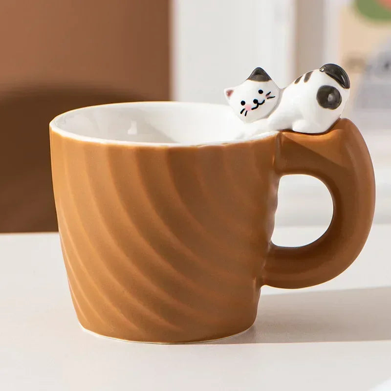 Brown mug with a cat-shaped handle and two small cat figurines on a light background