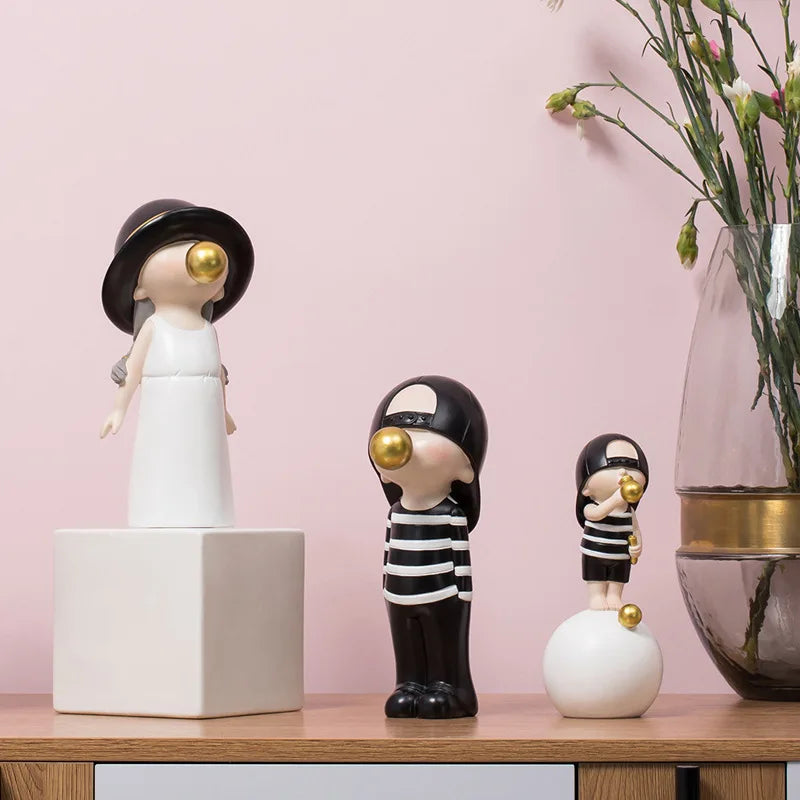 Three decorative figurines blowing a bubblegum on a wooden surface with a pink background