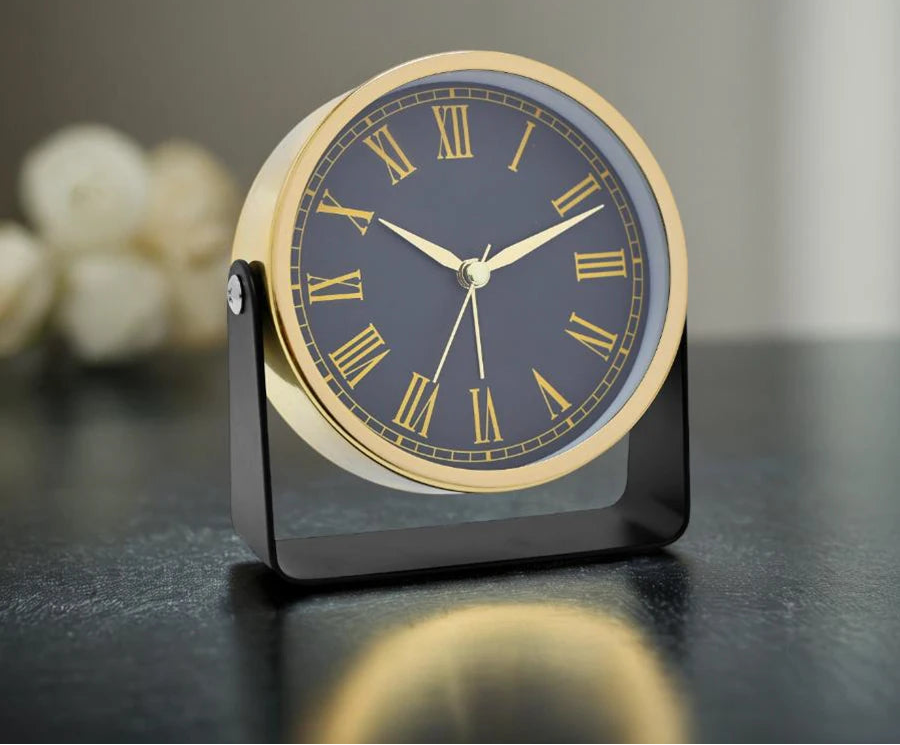 Table alarm clock with gold shell and dark face on a reflective surface
