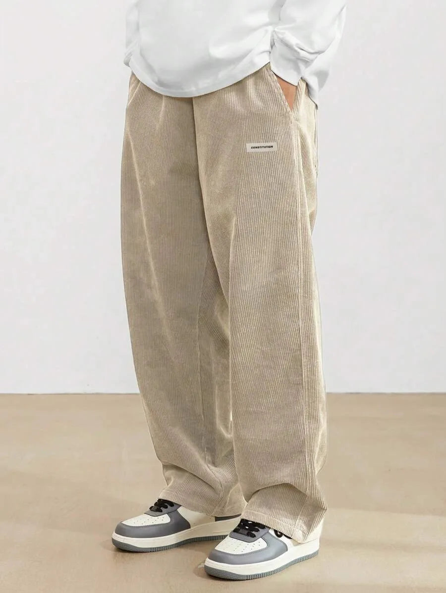 Person wearing beige corduroy pants and white sneakers on a plain background