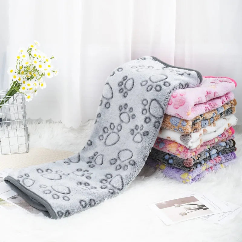 Stack of folded pet blankets with a gray one featuring paw prints on a light surface.