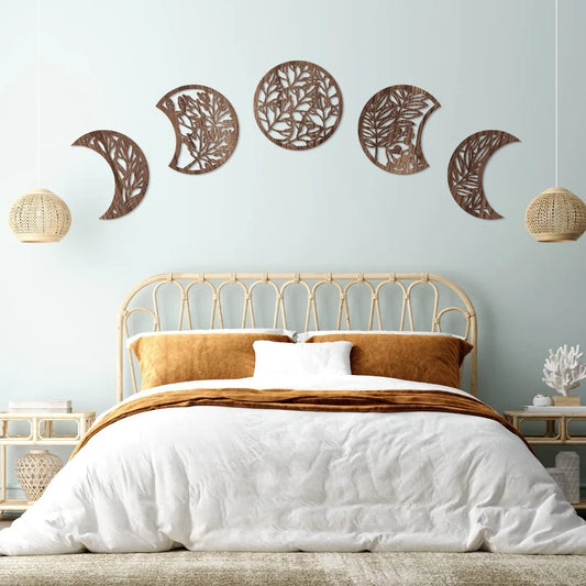 Wooden moon phase wall art set with botanical cut-out design hanging above bed in Nordic boho bedroom decor