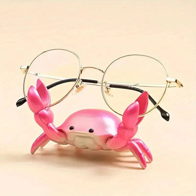 Pink crab-shaped glasses holder with a pair of glasses on a beige background