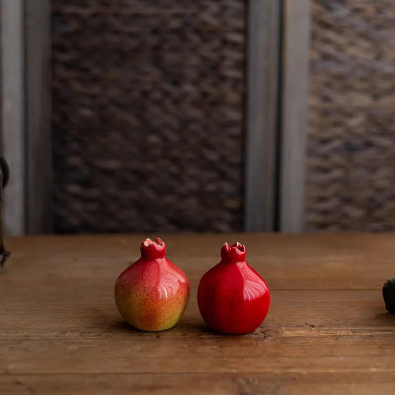 Two pomegranate-shaped objects on a wooden surface with a textured wall background.