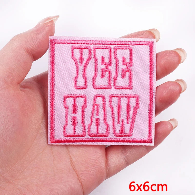 Pink patch with 'YEE HAW' text held in a hand, on a white background