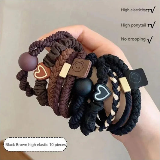 Hand holding a set of black and brown hair ties with decorative elements on a neutral background.