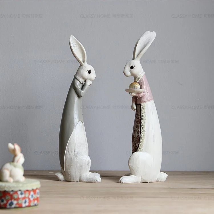 Two decorative rabbit figurines on a wooden surface with a gray background