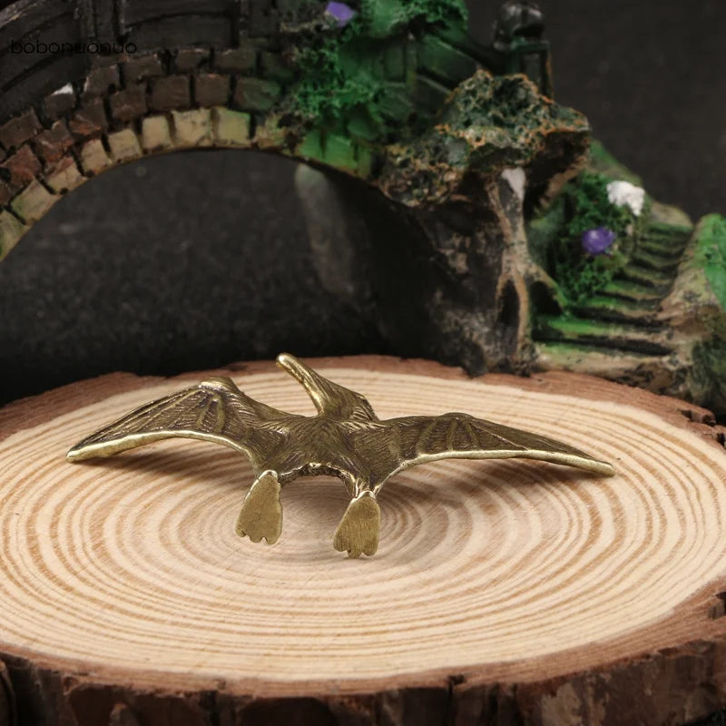 Bronze pterodactyl figurine on a wooden surface with a fantasy landscape in the background