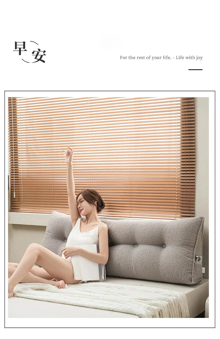 Woman sitting on a bed with a large pillow, wooden blinds in the background