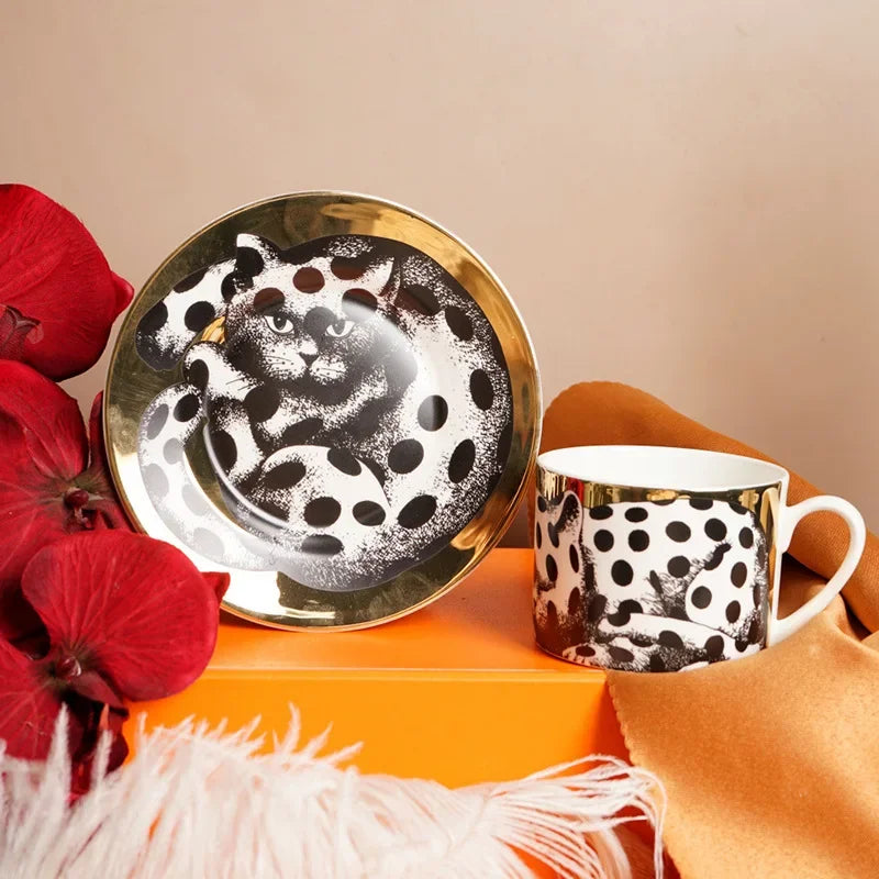 Decorative plate with a cat design and matching mug on an orange surface with red flowers.