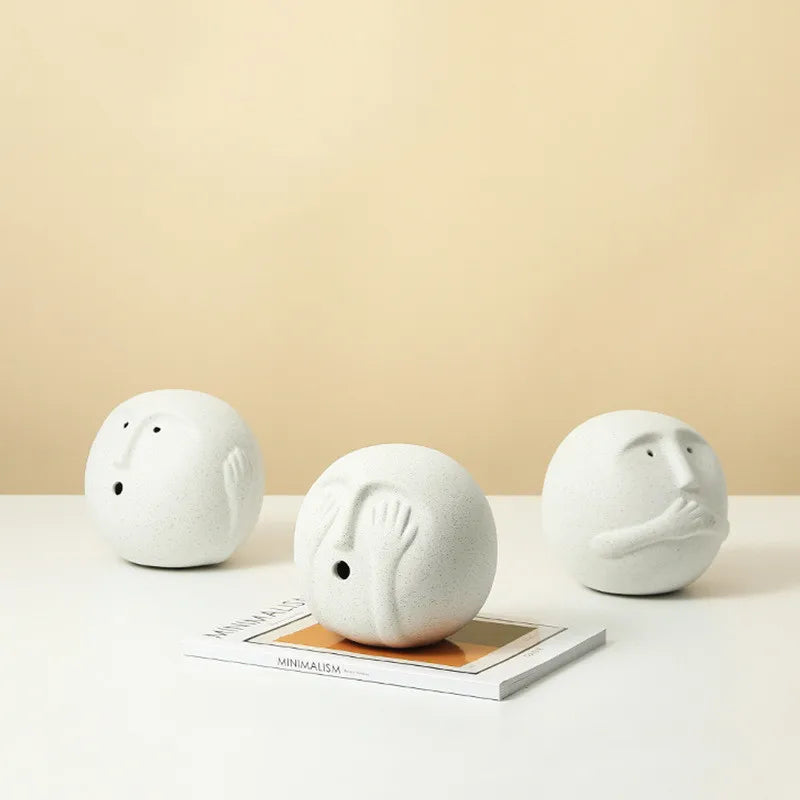 Three white ceramic face sculptures on a beige background