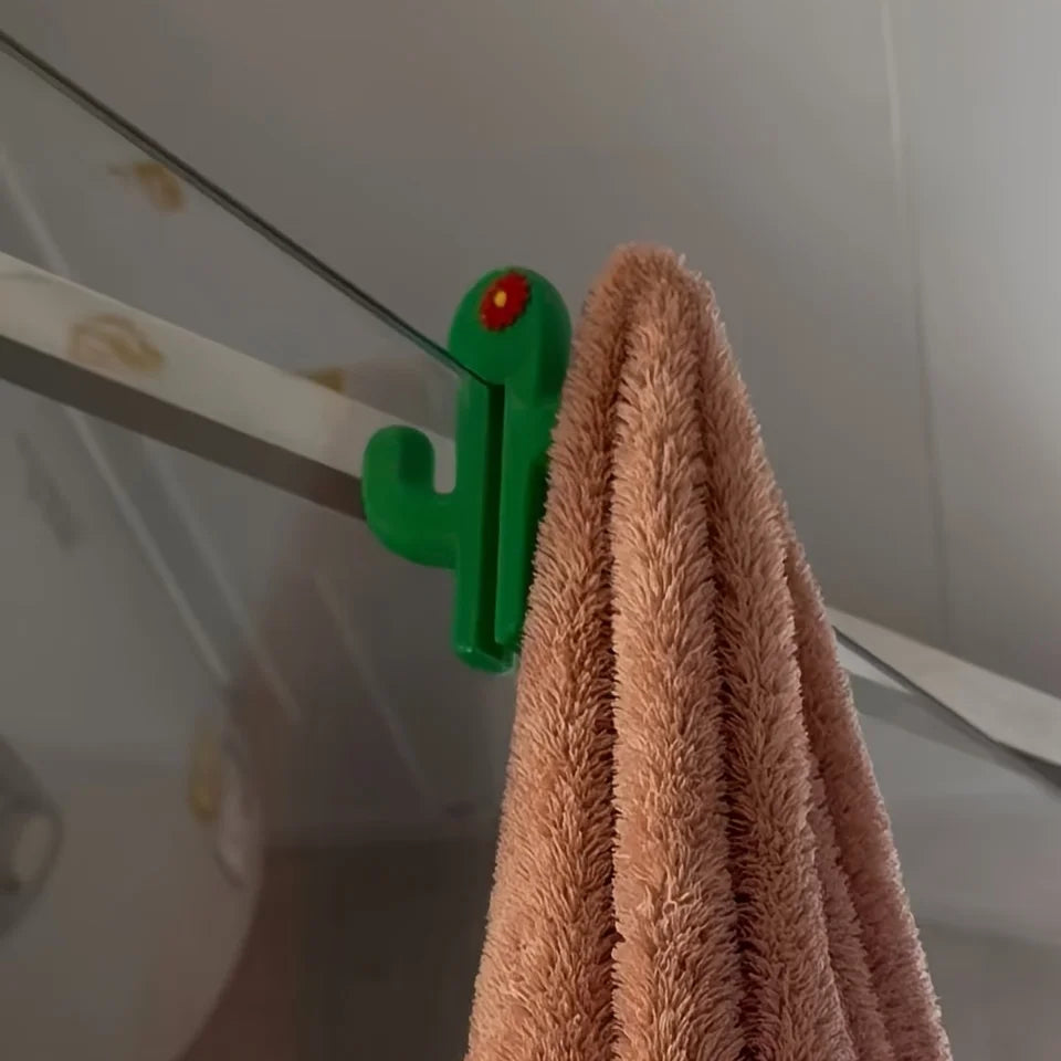 Brown towel hanging on a green cactus-shaped hook against a white wall.