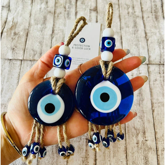 Hand holding two blue evil eye charms on a wooden surface
