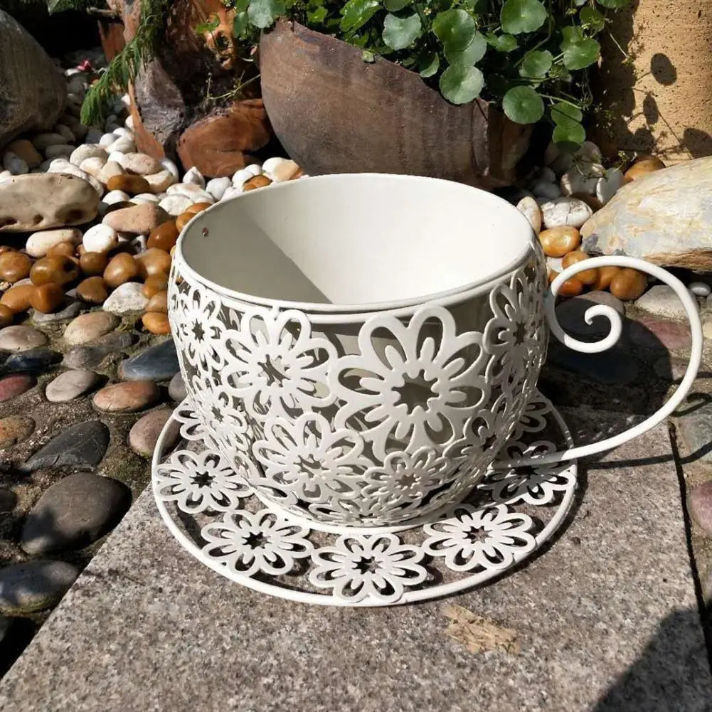 Decorative white metal teacup and saucer with floral patterns on a stone surface.