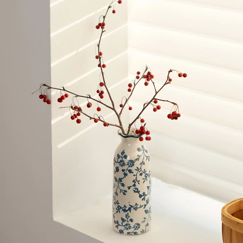 Decorative vase with blue floral patterns and red berries on a white surface.