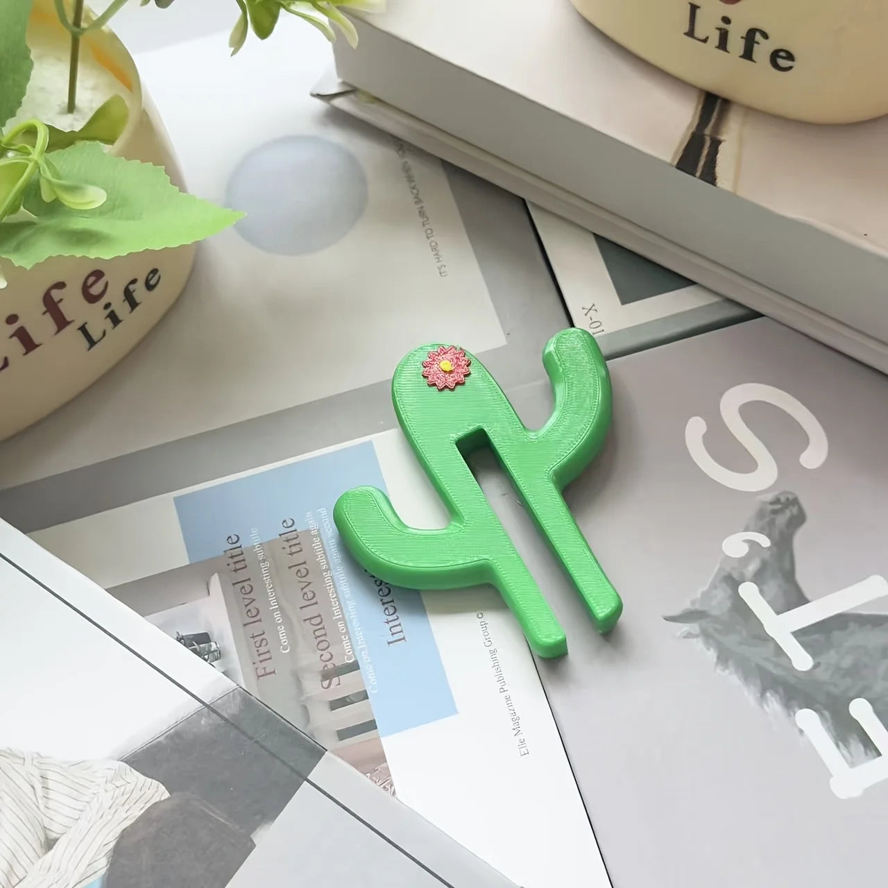 Green cactus-shaped object on a surface with books and a plant