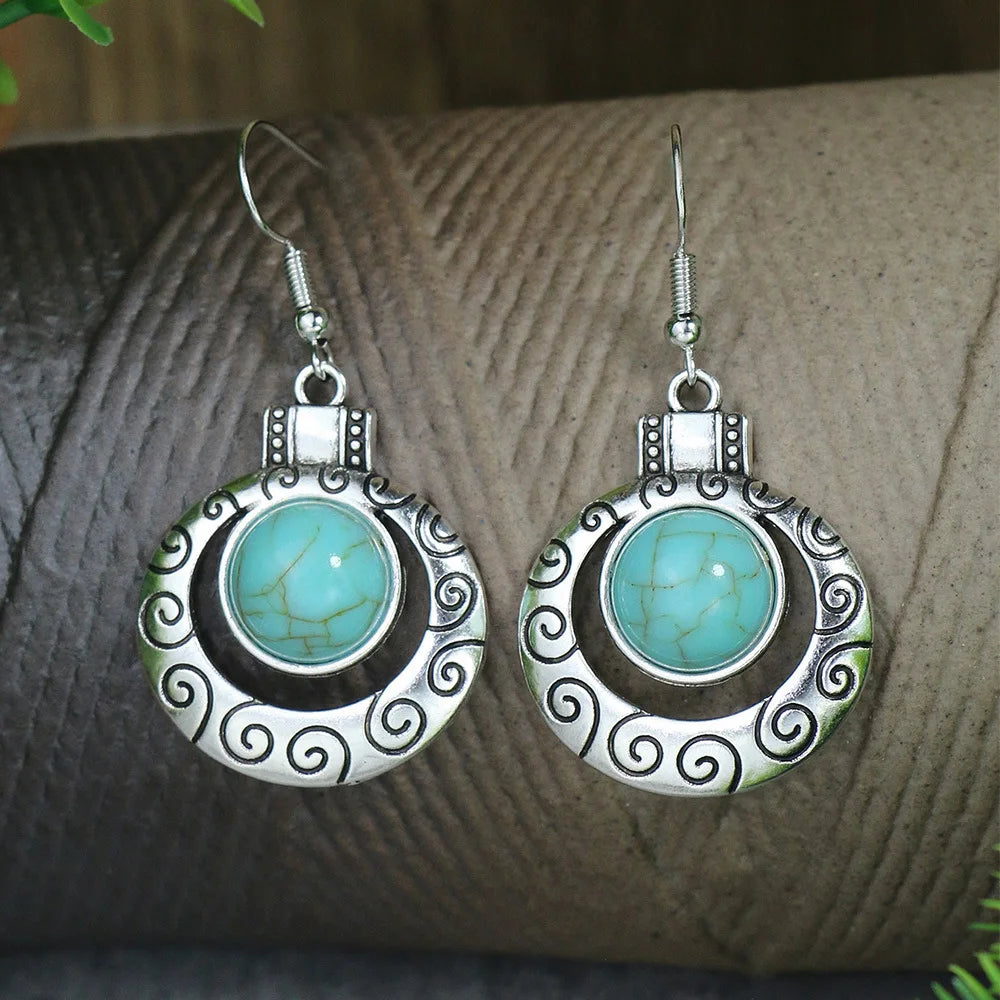 Pair of silver earrings with turquoise stones on a textured surface