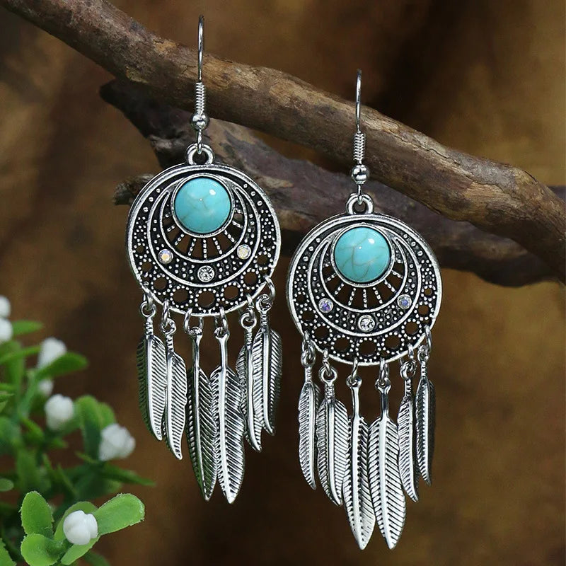 Pair of earrings with turquoise stones and feather details on a branch.