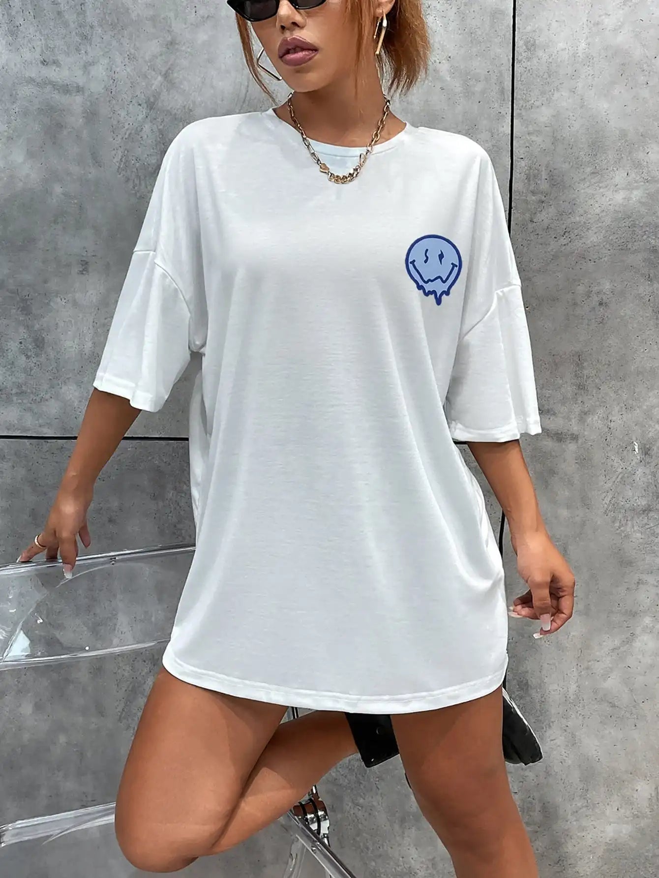 Person wearing a white oversized t-shirt with a blue graphic design against a gray wall.