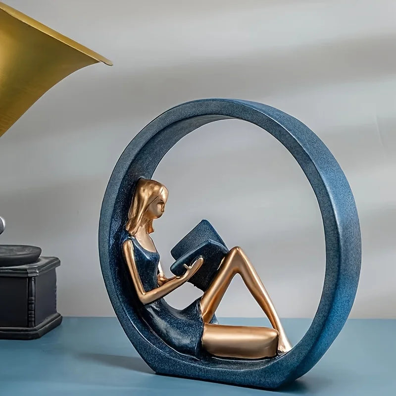 Statue of a woman reading a book inside a circular sculpture on a blue surface.