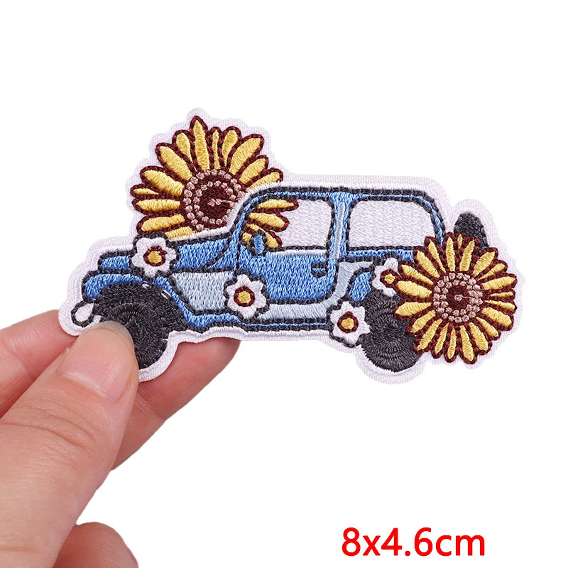 Embroidered patch of a car with sunflowers held by a hand on a white background
