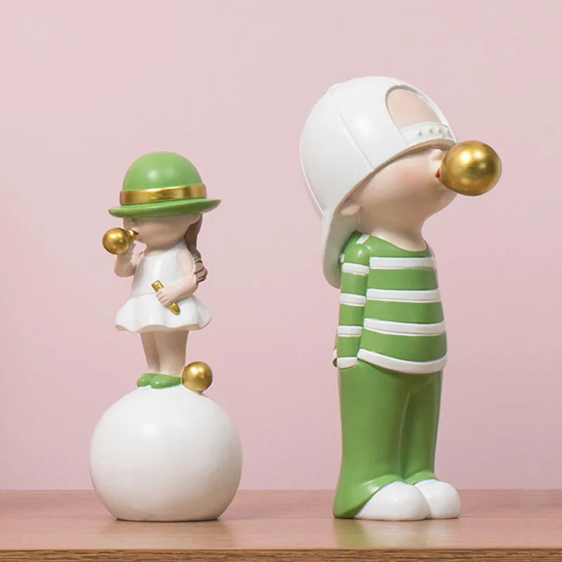 Two decorative figurines, one in a green hat and white dress, the other in a striped outfit with a gold bubblegum, on a pink background.
