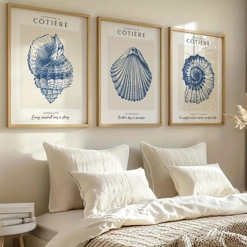 Set of three blue coastal shell canvas prints displayed above a bed featuring vintage nautical shell illustrations and beach-inspired wall décor.