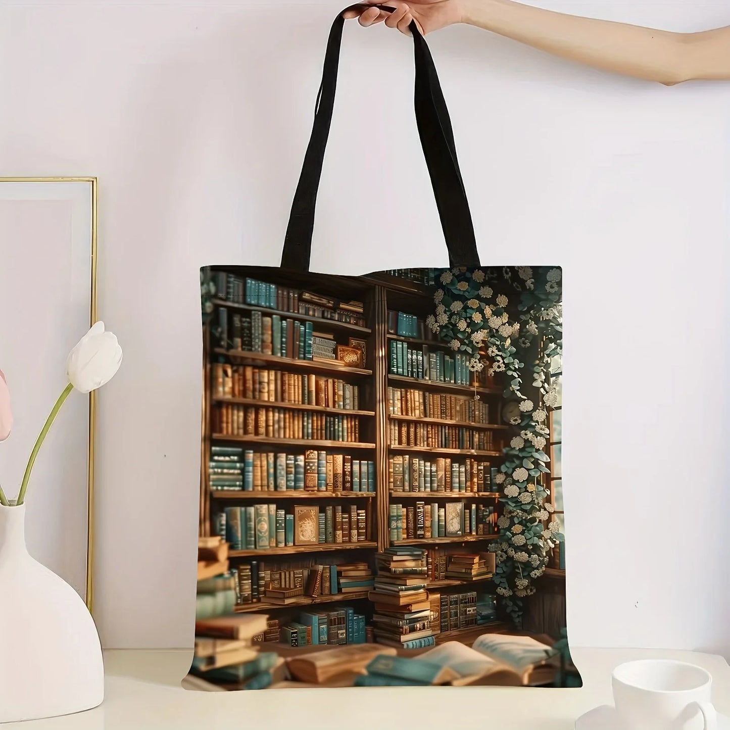Tote bag with a design of a bookshelf filled with books held by a hand against a white background.