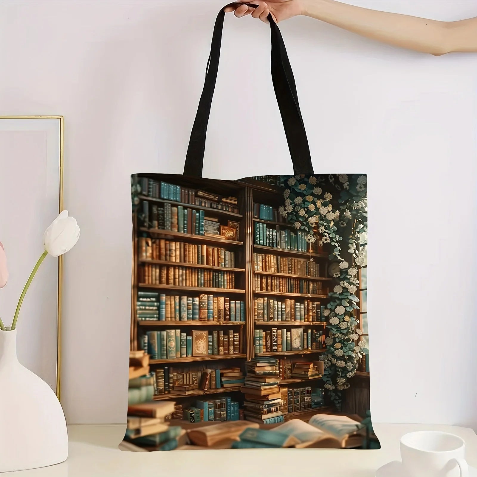 Tote bag with a design of a bookshelf filled with books held by a hand against a white background.