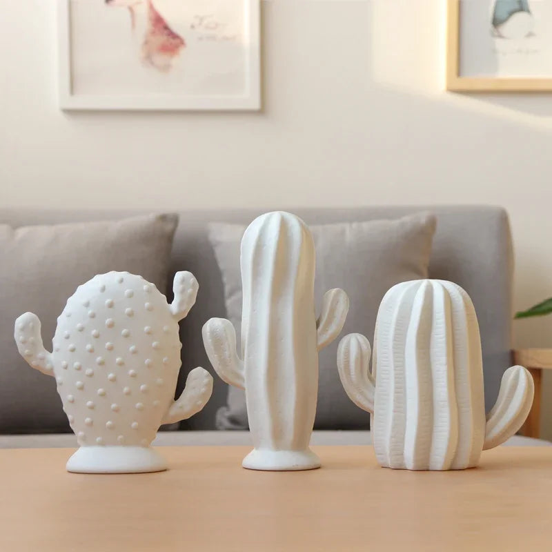 Three white ceramic cactus sculptures on a table with a blurred background of a living room.
