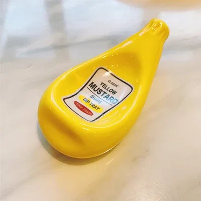 A yellow mustard-shaped dip tray with a white and blue label reading 'Classic Yellow Mustard Lip Balm' on a light marble surface.